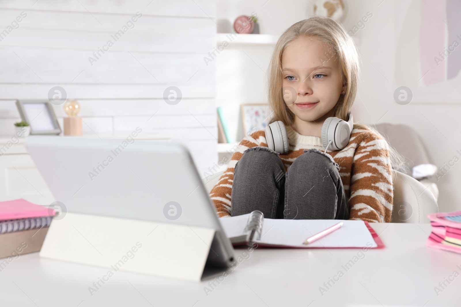 Photo of Cute little girl with modern tablet studying online at home. E-learning