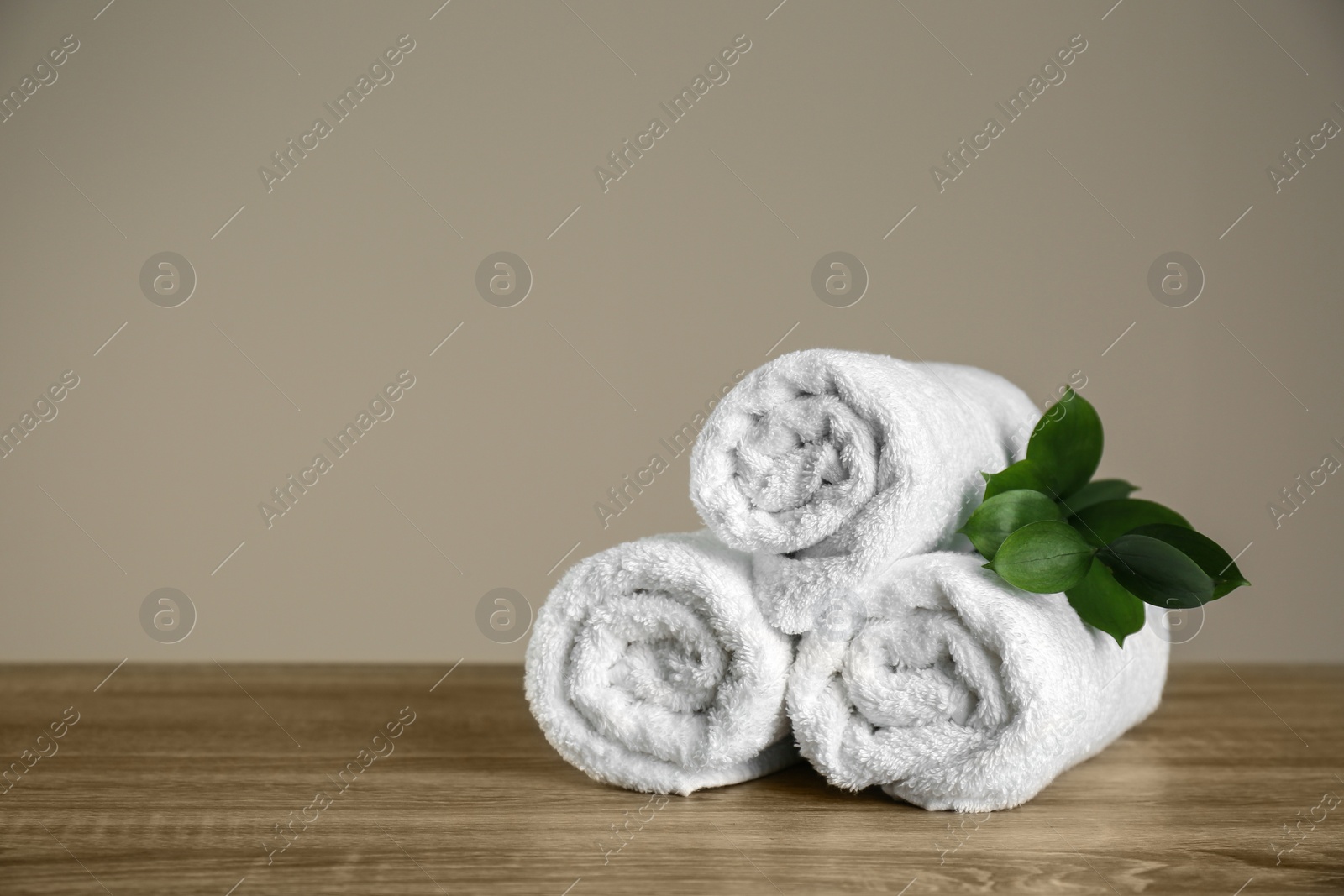 Photo of Clean rolled towels and green branch on wooden table. Space for text