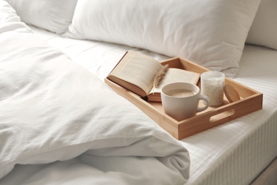 Photo of Cup of aromatic coffee, book and candle on bed with soft blanket indoors