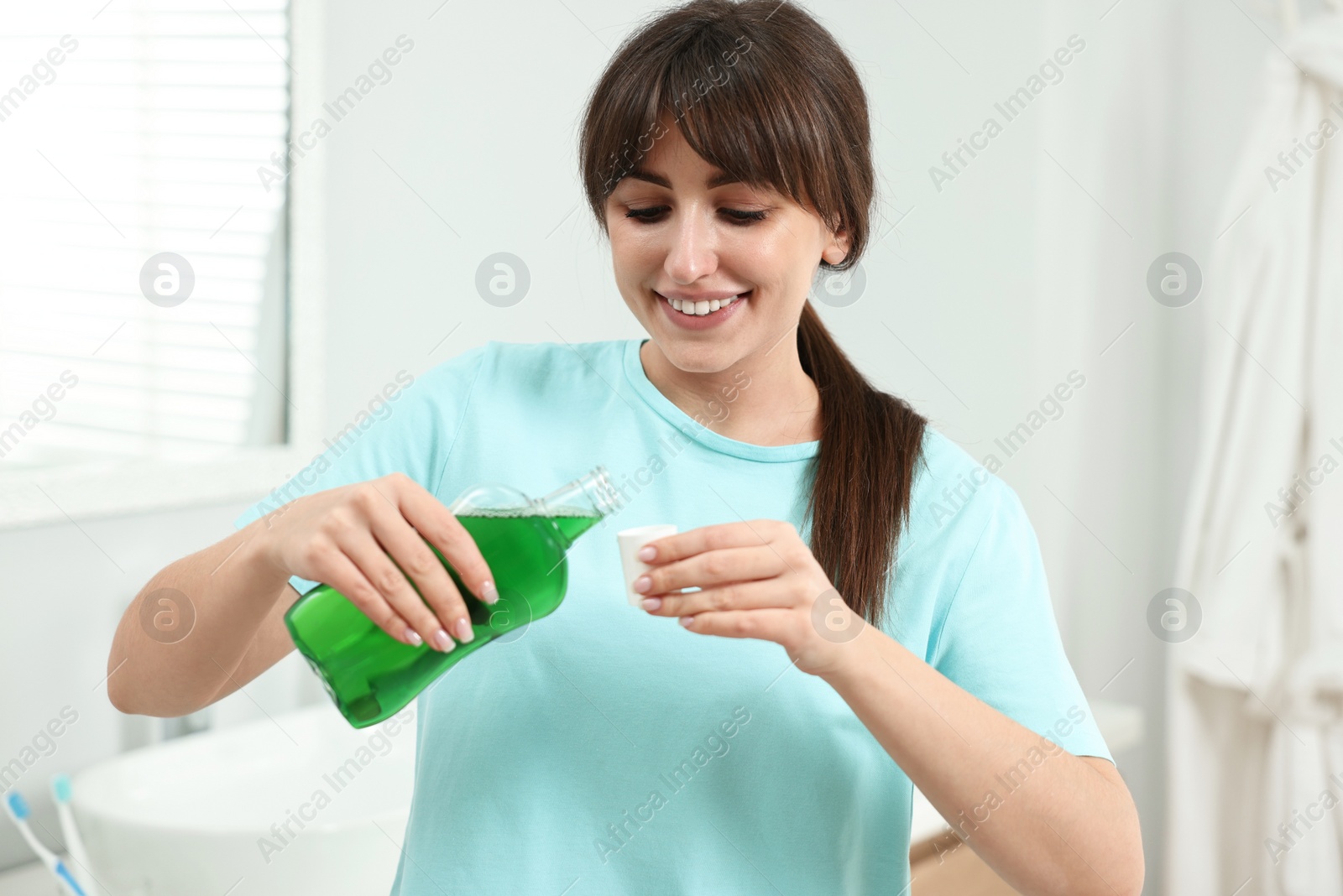 Photo of Young woman using mouthwash in bathroom. Oral hygiene