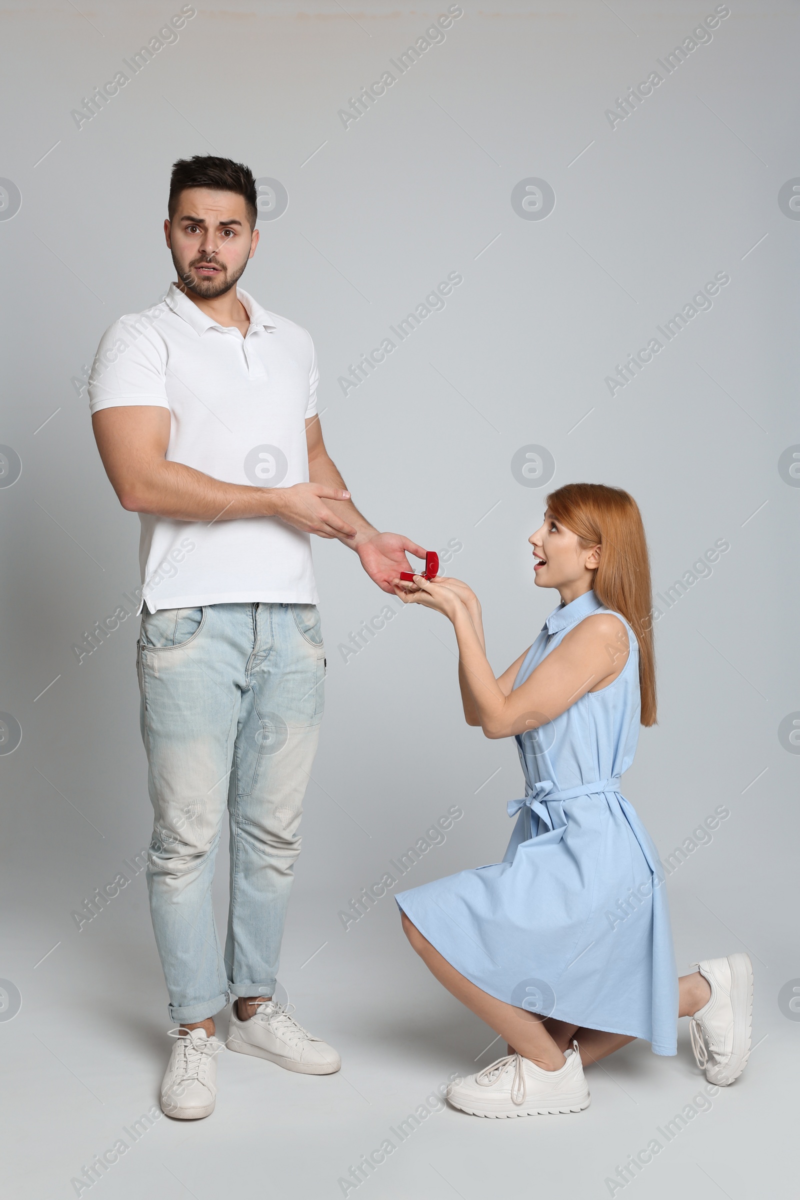 Photo of Young woman with engagement ring making marriage proposal to her boyfriend on light grey background