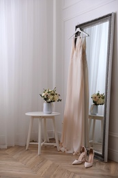 Elegant wedding dress hanging on large mirror in room