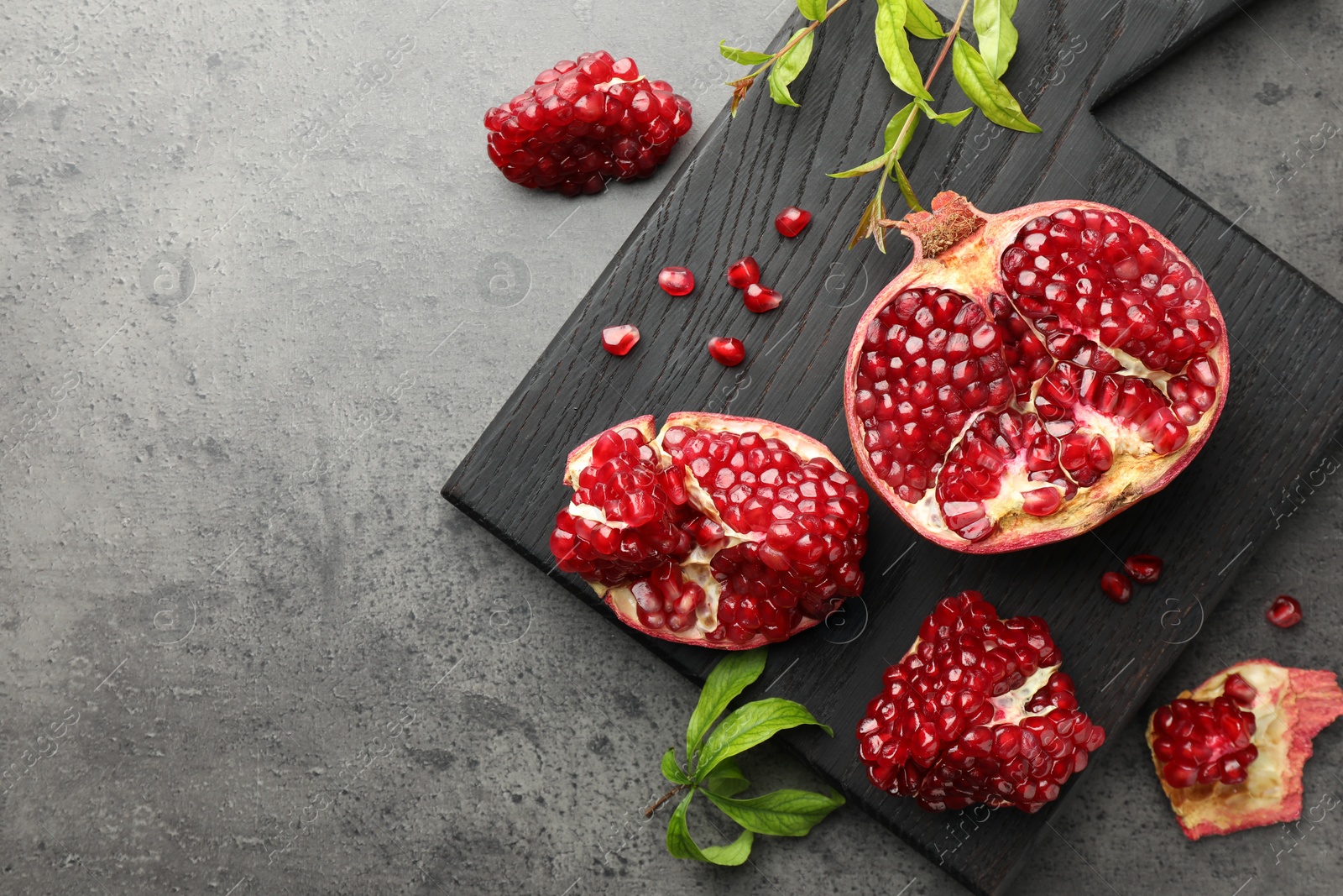 Photo of Cut fresh pomegranate and green leaves on grey table, top view. Space for text