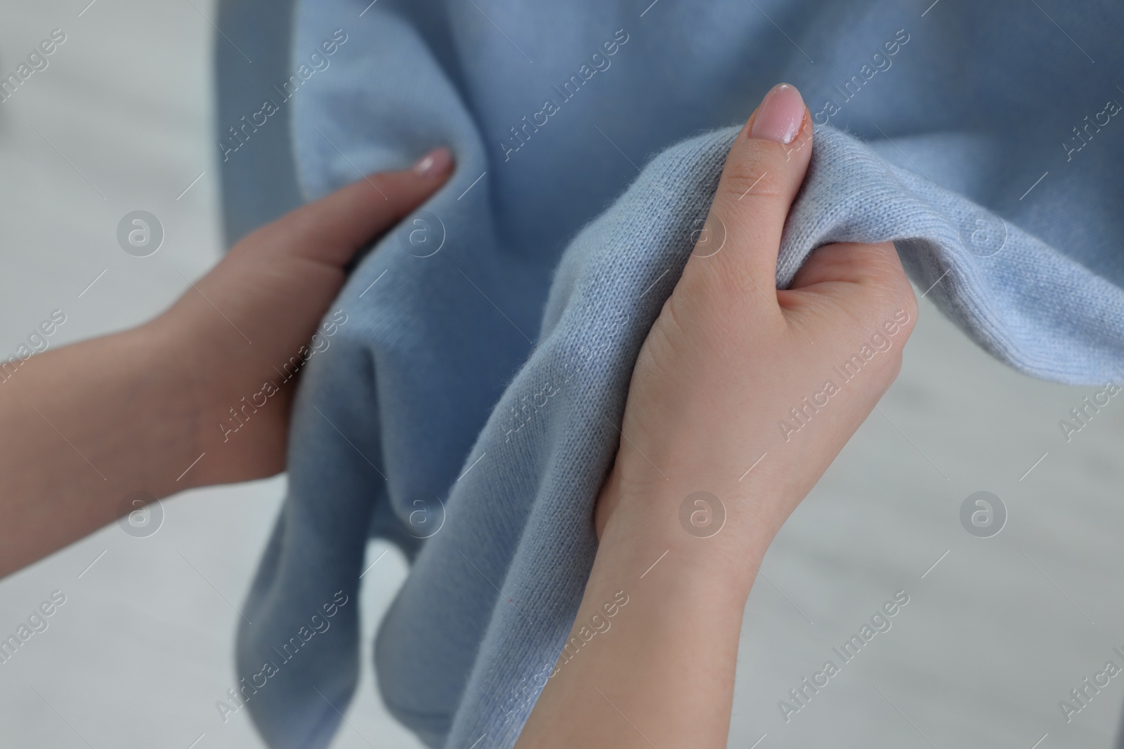 Photo of Woman touching clothes made of soft light blue fabric indoors, closeup