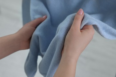 Woman touching clothes made of soft light blue fabric indoors, closeup