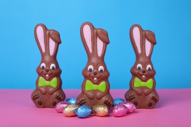 Chocolate Easter bunnies and eggs on pink table against light blue background
