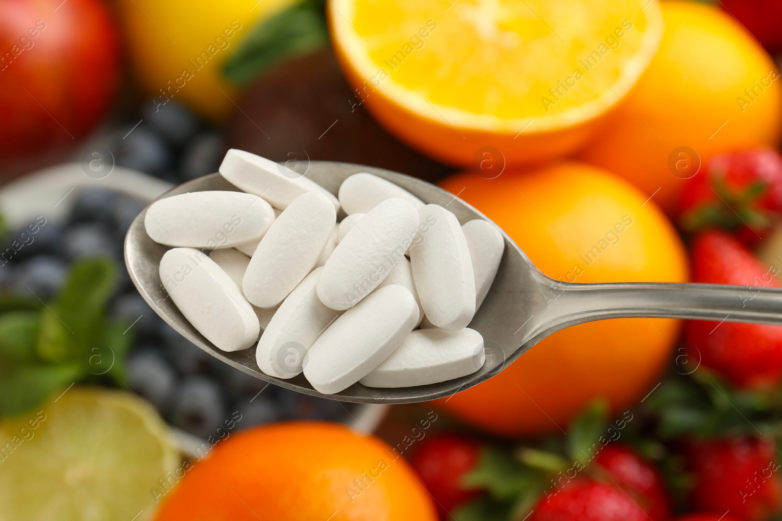 Photo of Vitamin pills in spoon over fresh fruits, closeup