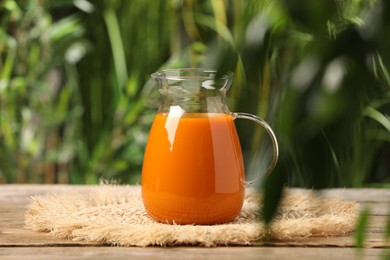 Photo of Tasty carrot juice on wooden table outdoors