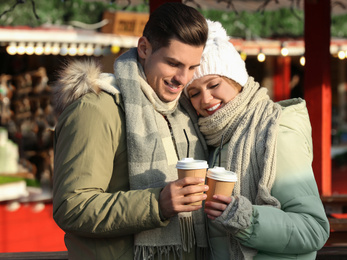 Photo of Happy couple in warm clothes with drinks at winter fair. Christmas season