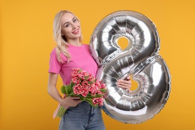 Happy Women's Day. Charming lady holding bouquet of beautiful flowers and balloon in shape of number 8 on orange background