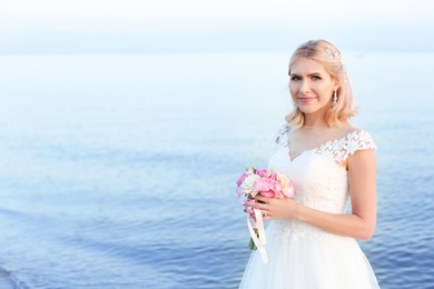 Happy bride holding wedding bouquet on beach. Space for text