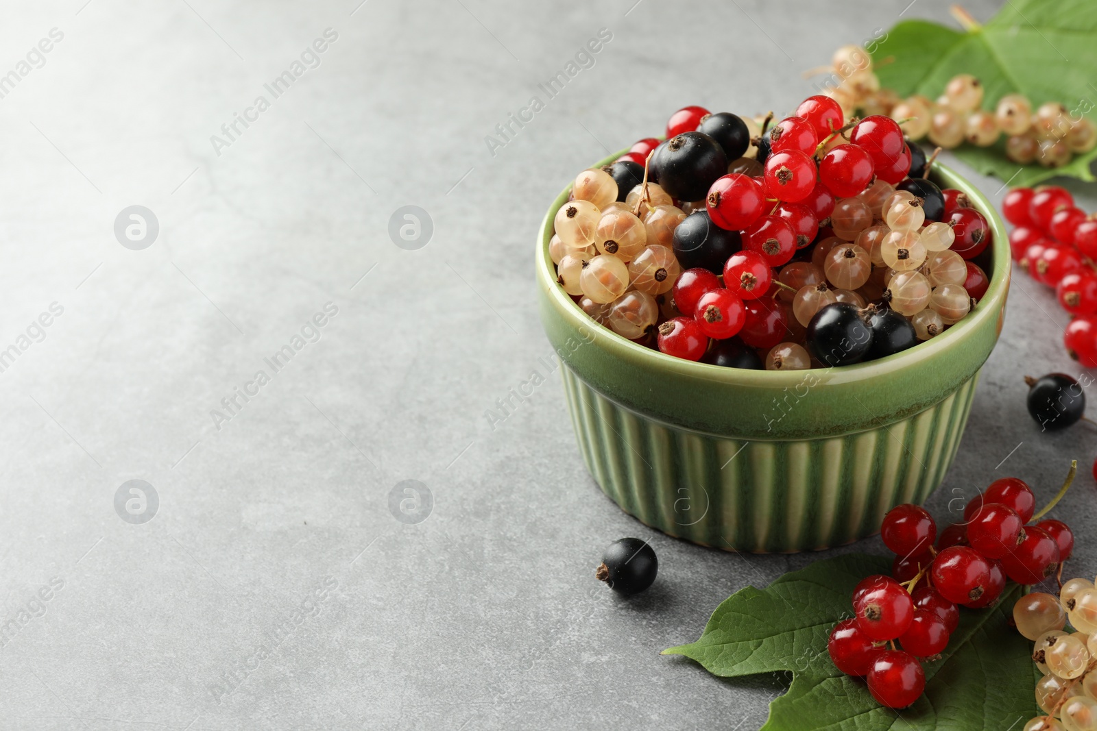 Photo of Different fresh ripe currants and green leaf on light grey table, space for text