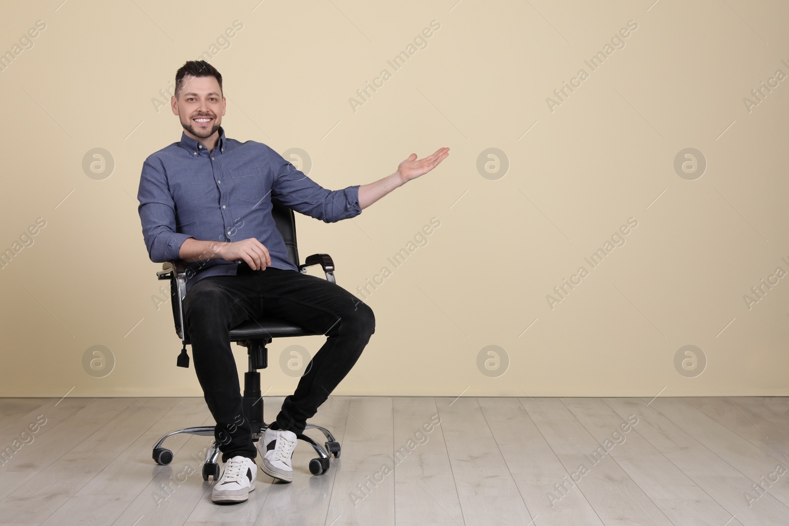 Photo of Handsome man sitting in office chair near beige wall indoors. Space for text