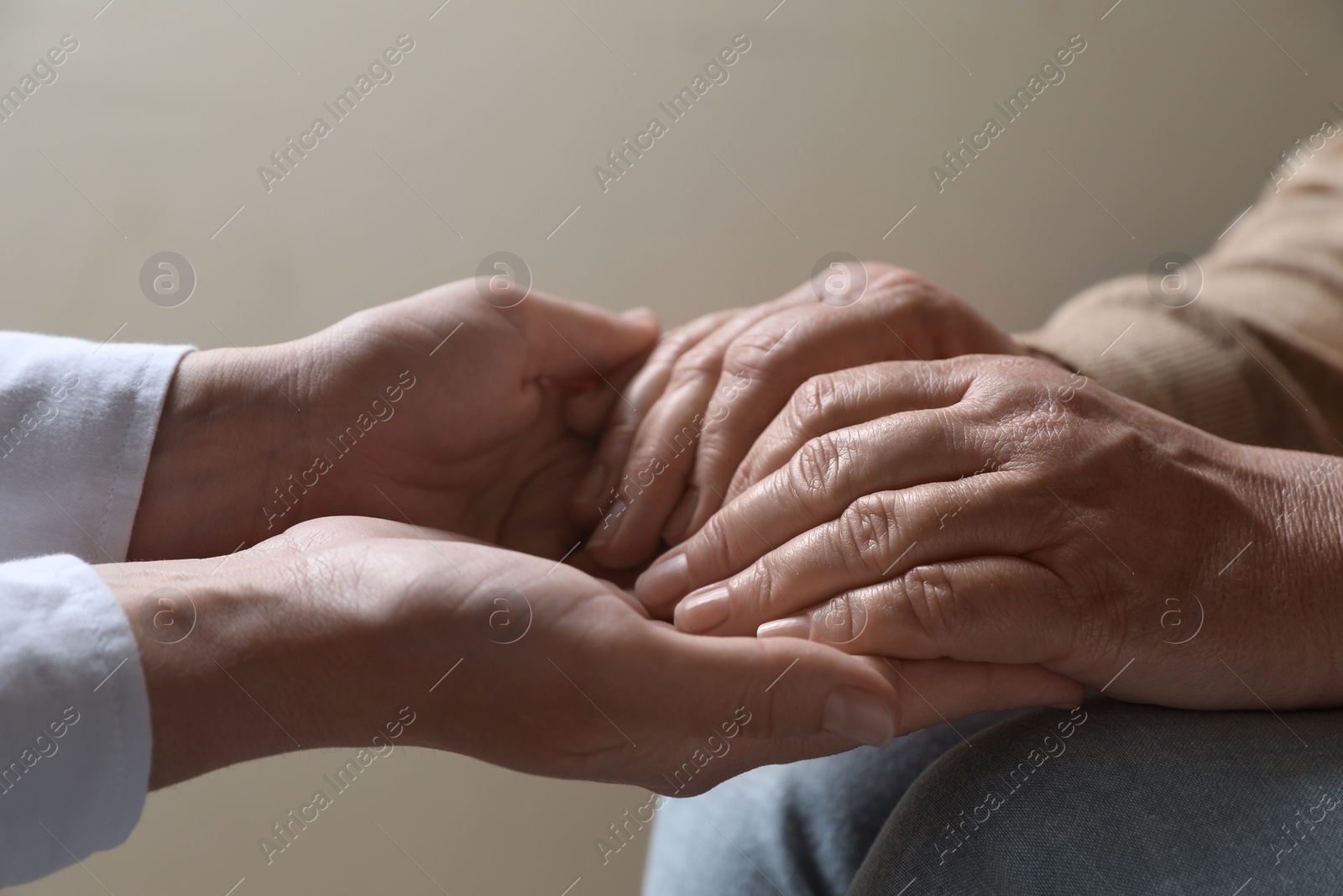 Photo of Woman holding hands with her mother on beige background, closeup