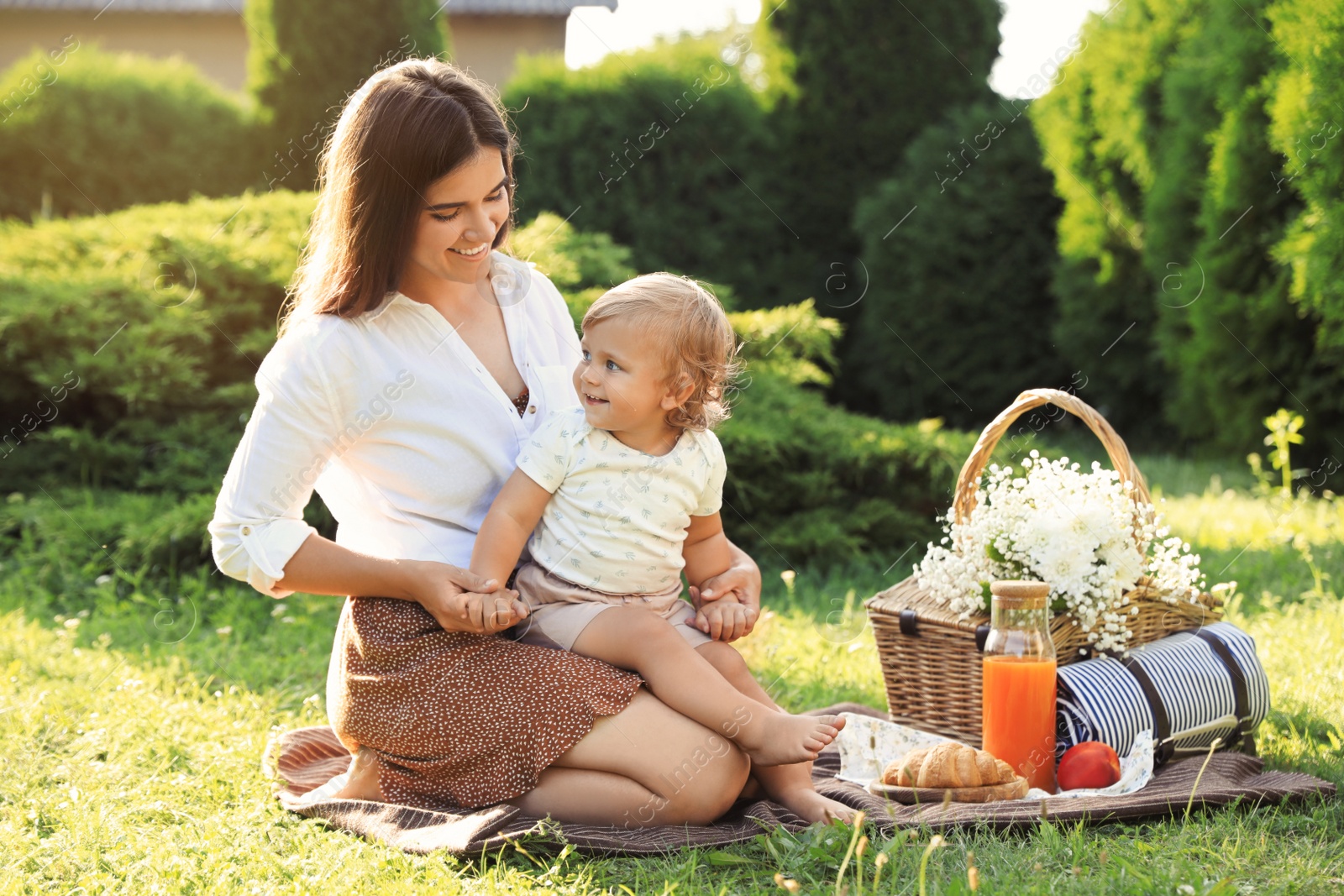 Photo of Mother with her baby daughter having picnic in garden on sunny day