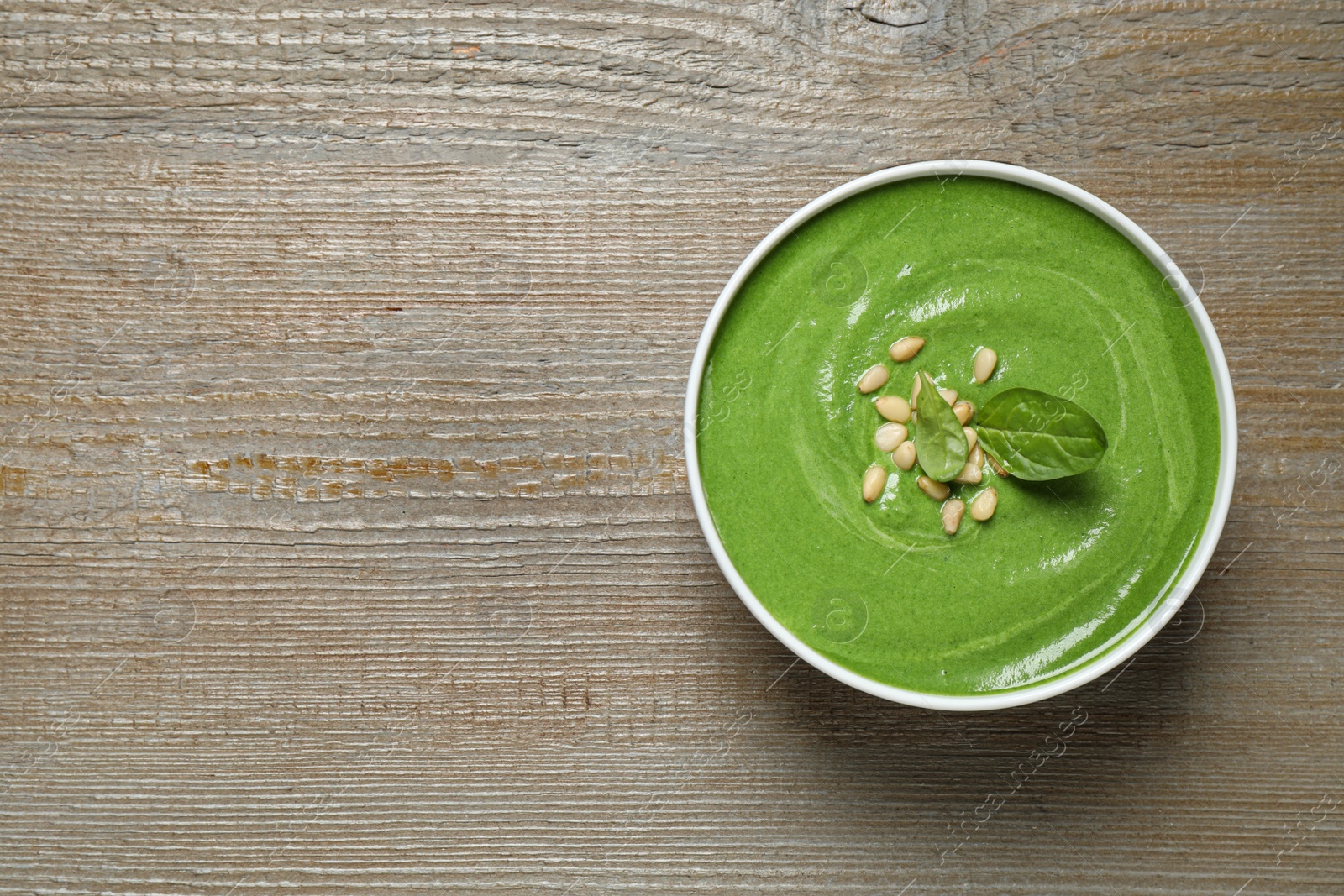 Photo of Bowl of healthy green soup with fresh spinach on wooden table, top view. Space for text