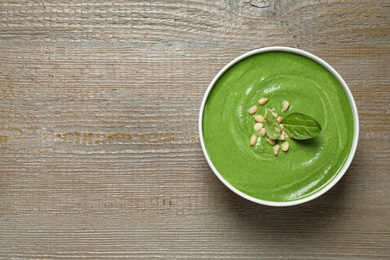 Bowl of healthy green soup with fresh spinach on wooden table, top view. Space for text