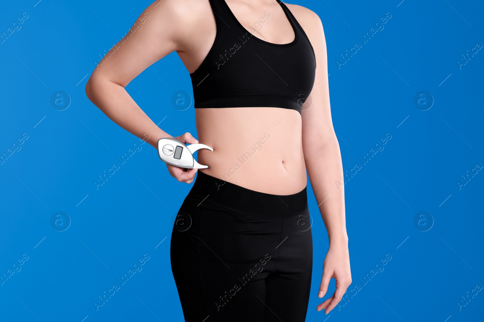 Photo of Young woman measuring body fat with caliper on blue background, closeup. Nutritionist's tool