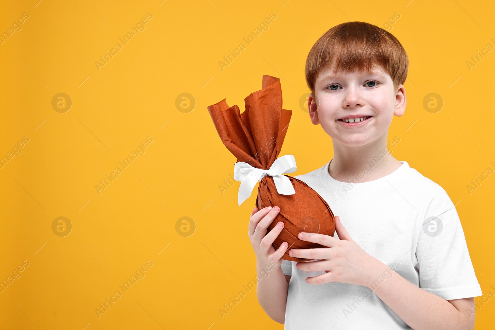 Photo of Easter celebration. Cute little boy with wrapped egg on orange background. Space for text