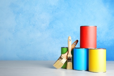 Photo of Cans with paint and brushes on table against color background. Space for text