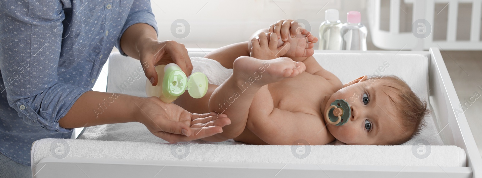 Image of Mother with bottle of massage oil near baby on changing table at home, closeup. Banner design