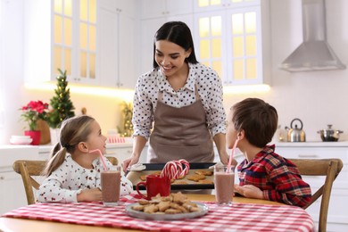 Photo of Mother giving her cute little children freshly baked Christmas cookies in kitchen