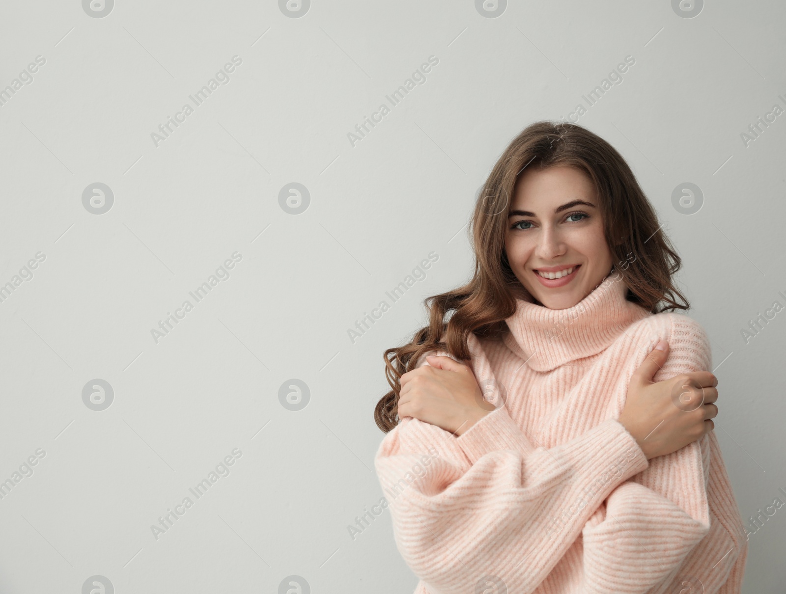 Photo of Beautiful young woman wearing warm pink sweater on light background. Space for text