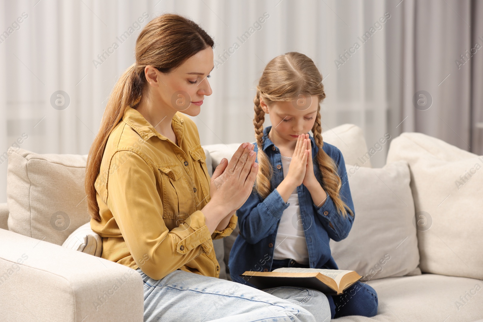 Photo of Girl and her godparent praying over Bible together on sofa at home