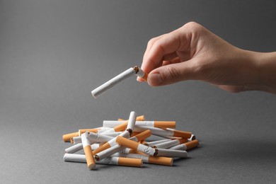 Photo of Stop smoking. Woman holding broken cigarette over pile on grey background, closeup