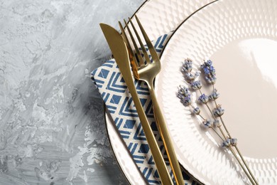 Photo of Clean plates, cutlery, napkin and lavender flowers on light grey textured table, top view. Space for text