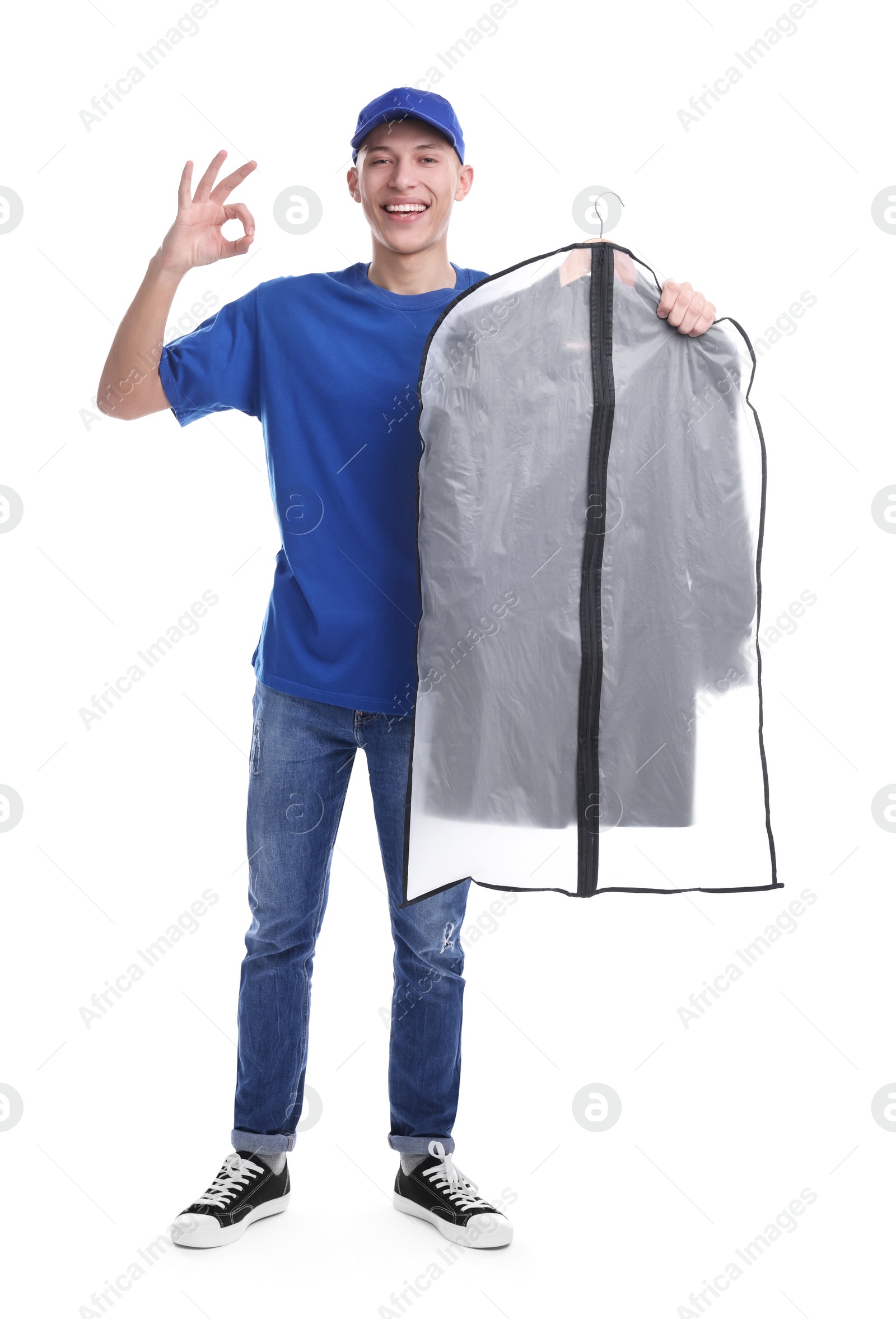 Photo of Dry-cleaning delivery. Happy courier holding garment cover with clothes and showing OK gesture on white background