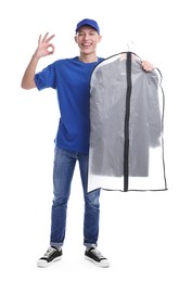 Dry-cleaning delivery. Happy courier holding garment cover with clothes and showing OK gesture on white background