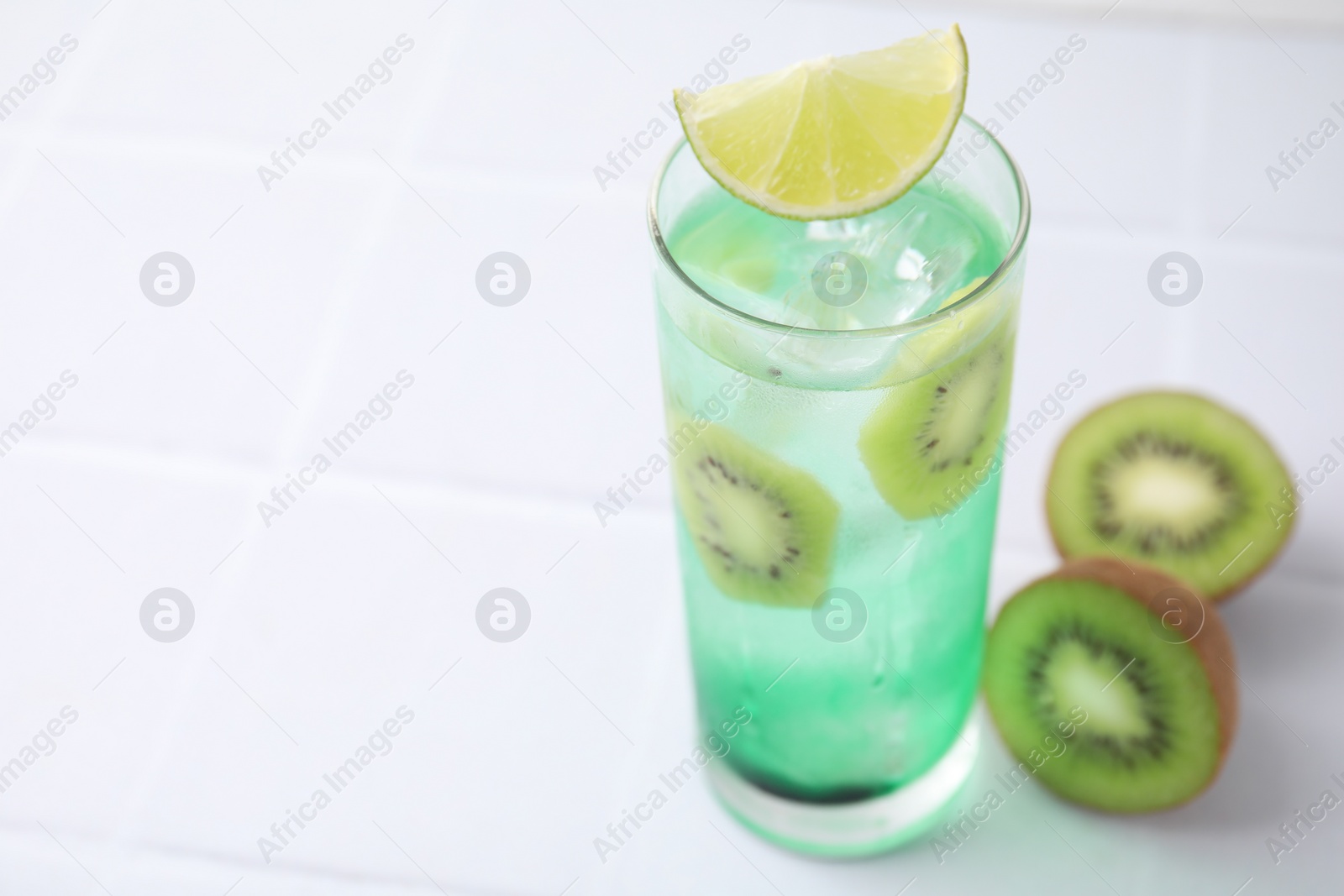 Photo of Glass of refreshing drink and cut kiwi on white table, closeup. Space for text