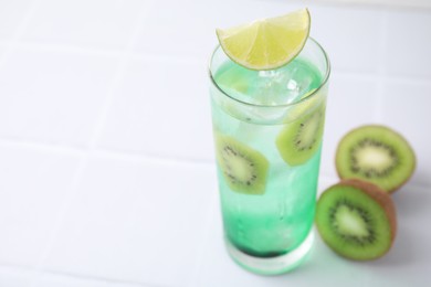 Photo of Glass of refreshing drink and cut kiwi on white table, closeup. Space for text