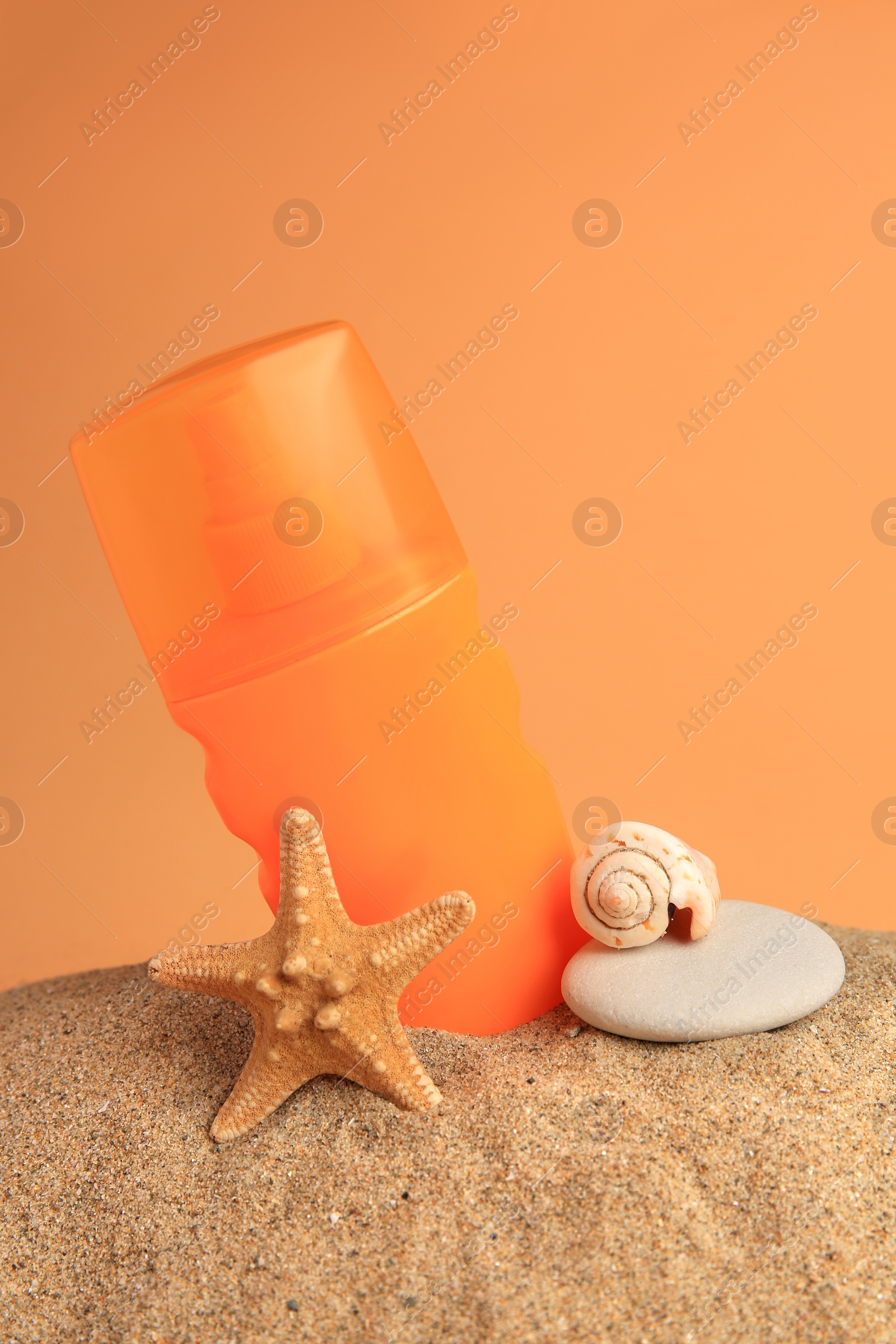 Photo of Sand with bottle of sunscreen, starfish, stone and seashell against orange background. Sun protection