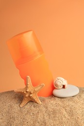 Sand with bottle of sunscreen, starfish, stone and seashell against orange background. Sun protection