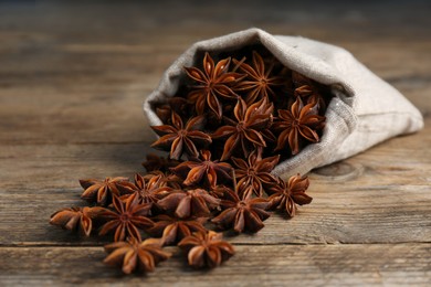Photo of Overturned bag with aromatic anise stars on wooden table, closeup