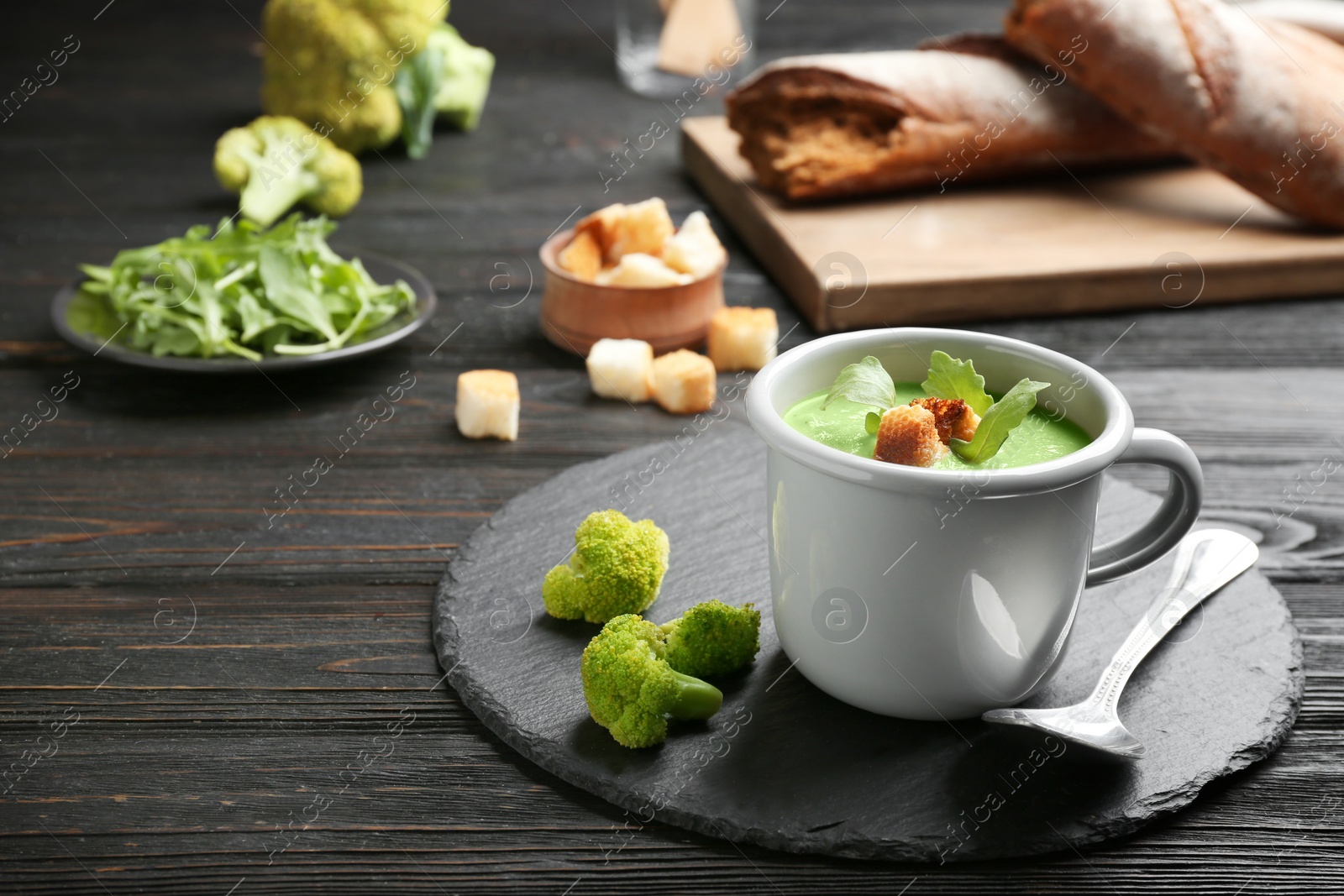 Photo of Cup of broccoli cream soup with croutons served on black wooden table, space for text