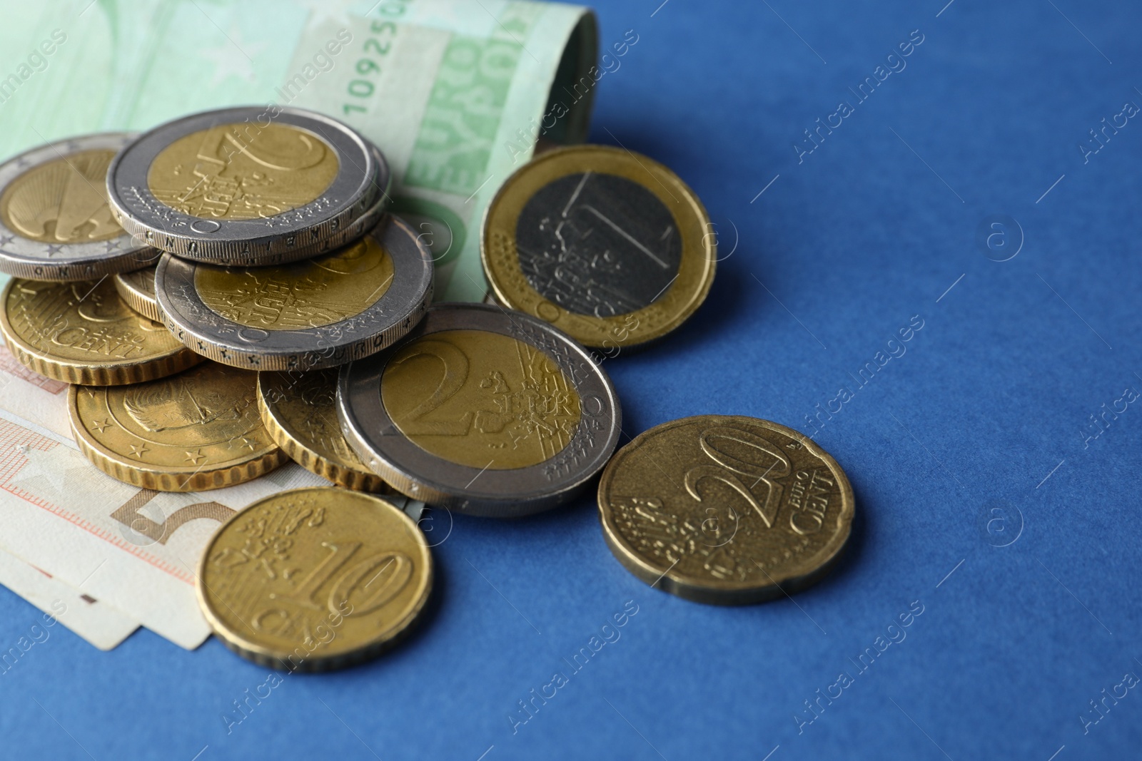Photo of Euro banknotes and coins on blue background, closeup