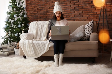 Photo of Beautiful young woman in hat opening gift box at home. Christmas celebration