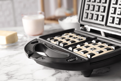 Belgian waffle maker with dough on white marble table, closeup