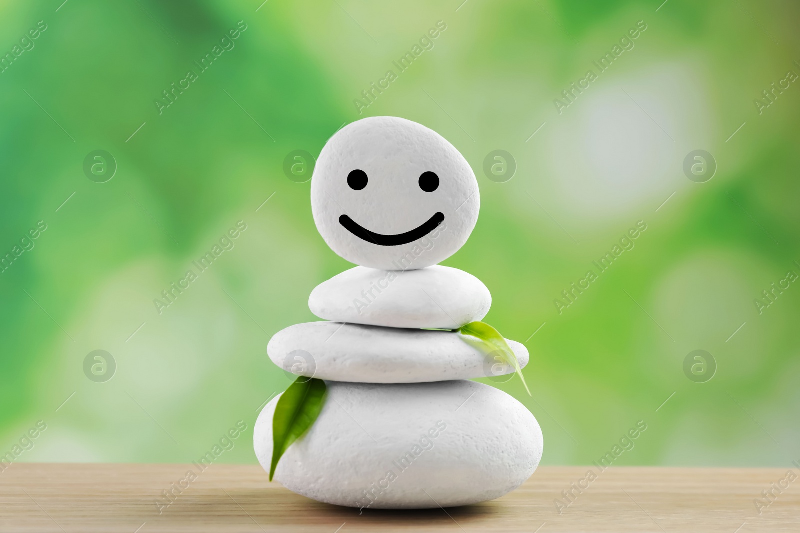 Photo of Stack of stones with drawn happy face and leaves on wooden table against blurred background. Zen concept