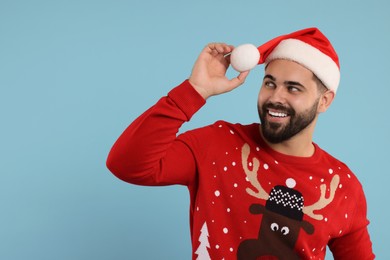 Photo of Happy young man in Christmas sweater and Santa hat on light blue background. Space for text