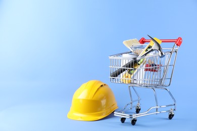 Photo of Small shopping cart with set of construction tools and hard hat on color background