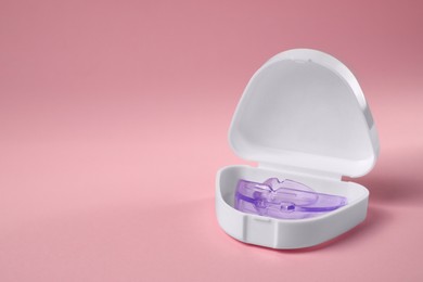 Photo of Transparent dental mouth guard in container on light pink background, space for text. Bite correction