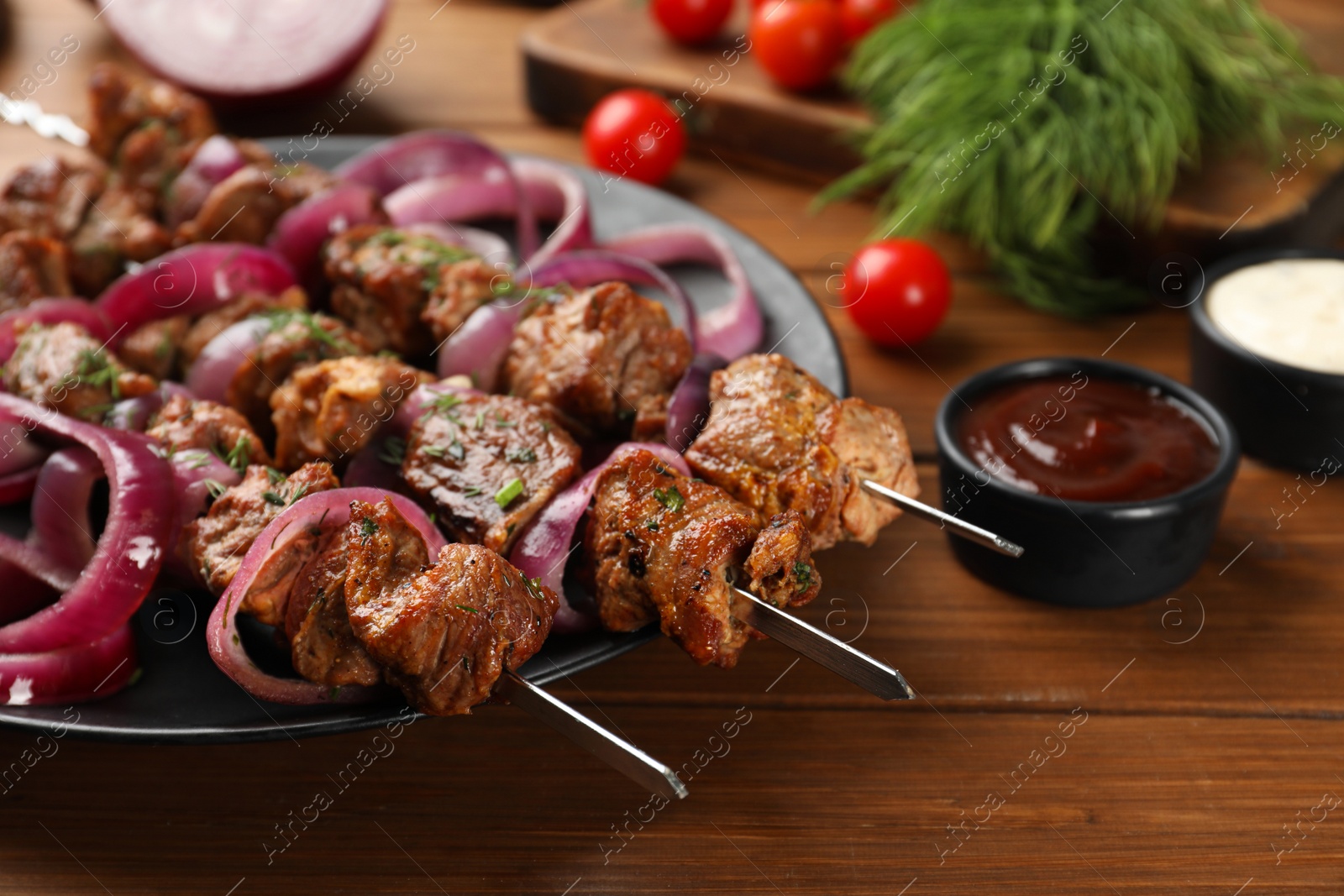 Photo of Metal skewers with delicious meat and onion served on wooden table, closeup