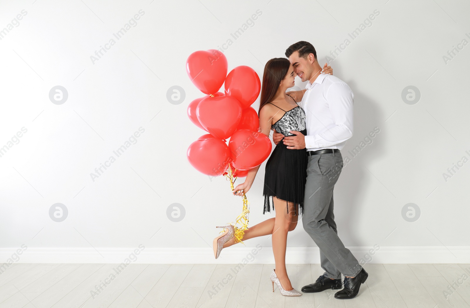 Photo of Beautiful couple with heart shaped balloons near light wall, space for text