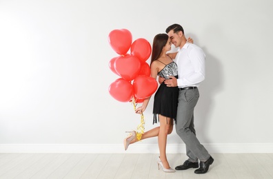 Photo of Beautiful couple with heart shaped balloons near light wall, space for text