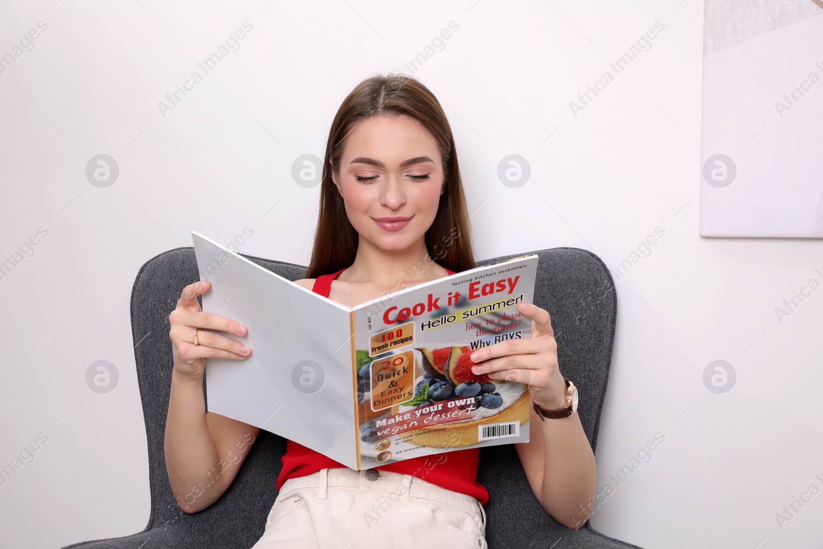 Photo of Young woman reading cooking magazine at home