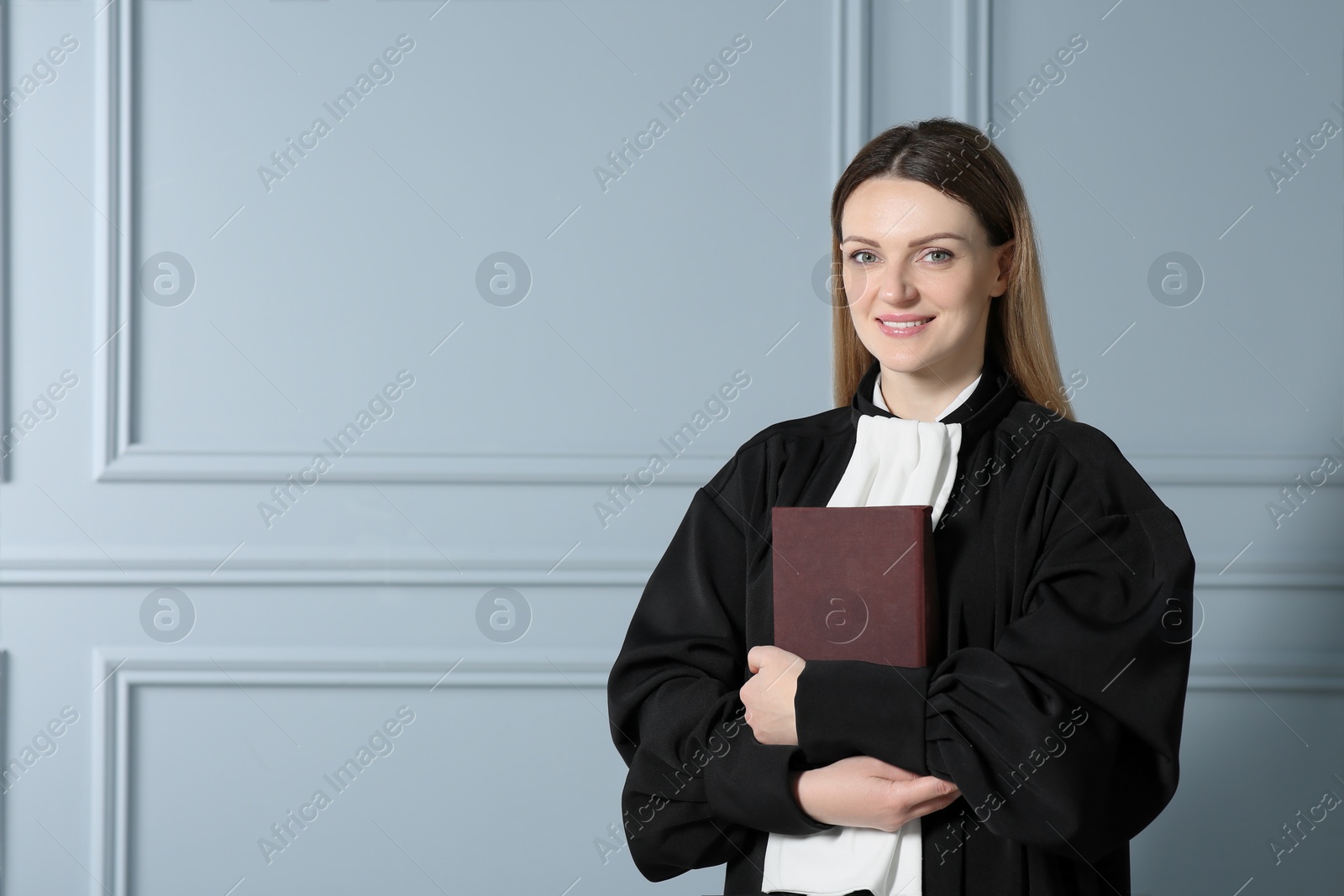 Photo of Portrait of smiling judge with book near grey wall. Space for text